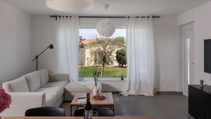 Una sala de estar moderna con un sofá, una mesa de centro, un televisor y un amplio ventanal con cortinas.