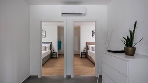 Habitación de hotel moderna con suelo de madera, paredes blancas y un espejo grande. Hay una planta en maceta sobre un tocador y una cama con una mesita de noche.