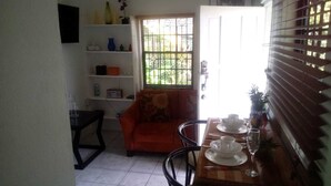 A dining area with a table set for two, a sofa, and a window with bars. - Henrietta's Seaview Studio (Gros Islet)