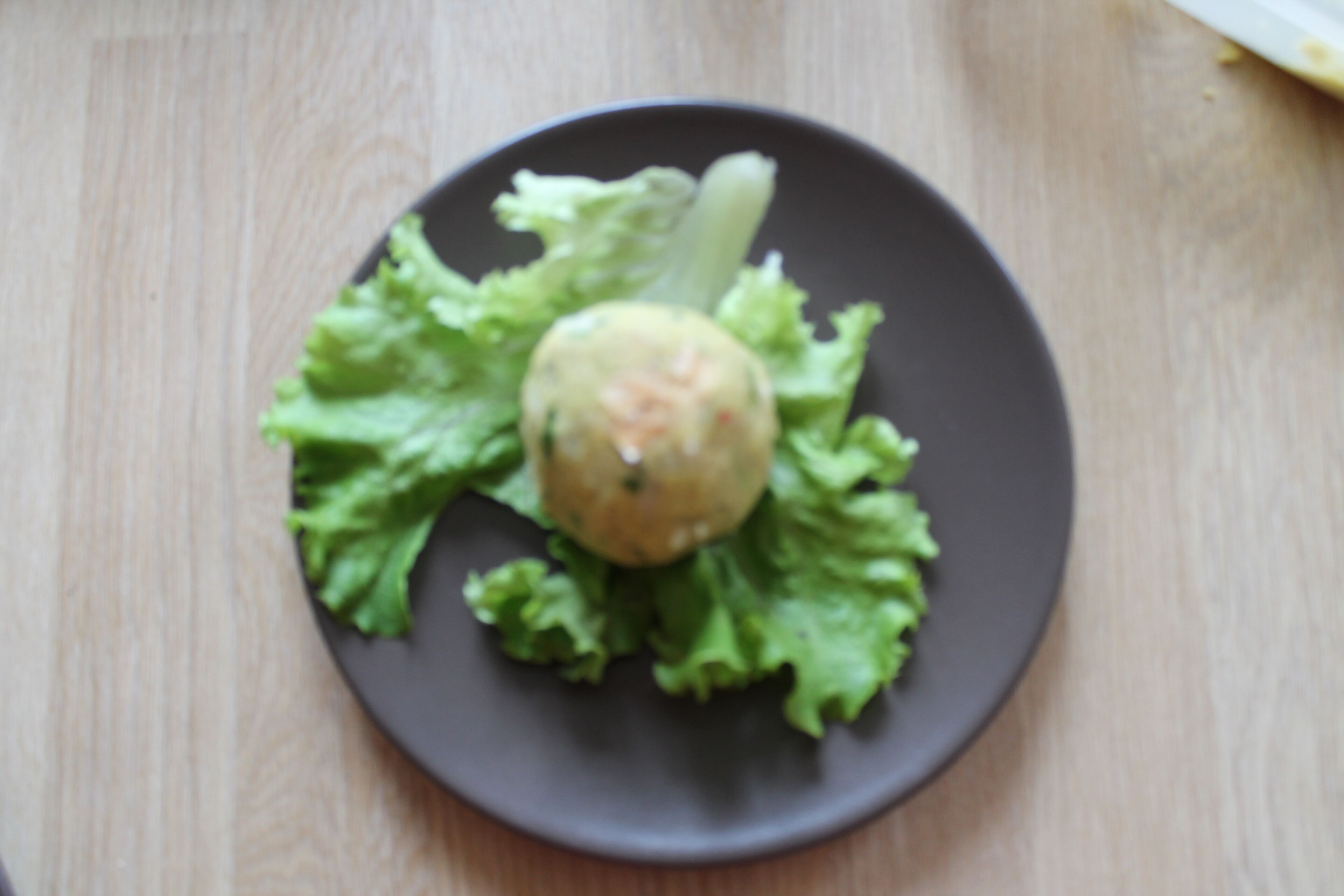 En tallerken med en rund madvare på et lag salatblade, placeret på en mørk tallerken.