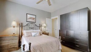 Une chambre à coucher avec un lit, des tables de chevet, une commode, un ventilateur de plafond et une porte.