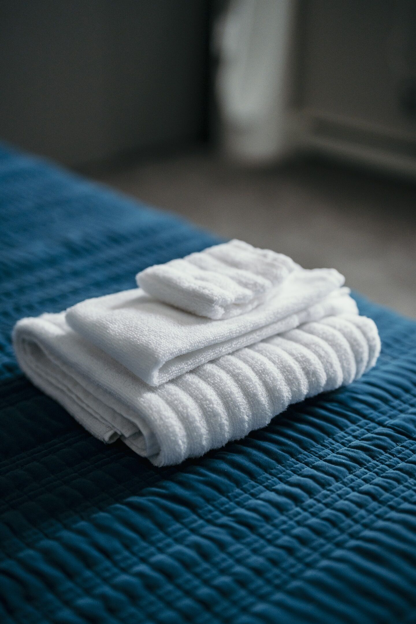 A neatly folded white towel on a blue quilted bedspread.