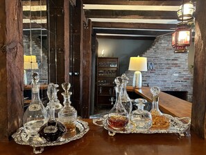 Una zona de bar con mostrador de madera, pared de ladrillo y estante con cristalería.