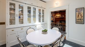 Et spiseområde med et hvidt bord og stole, en potteplante og et skab med glasdøre, der indeholder service.