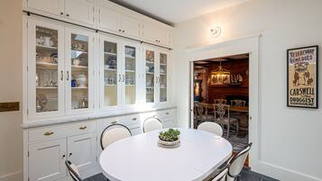 A dining area with a white table and chairs, a potted plant, and a cabinet with glass doors containing dishes.