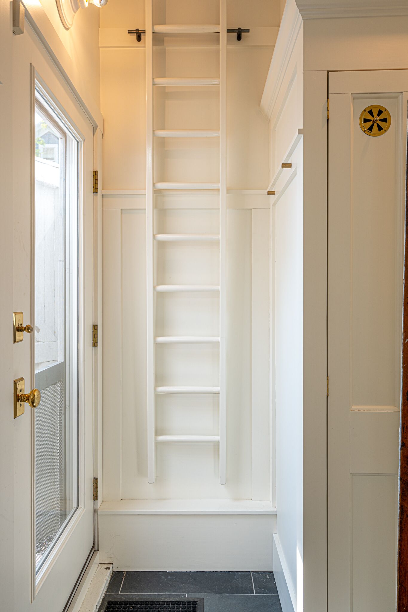 A narrow hallway with a white door on the left, a white door on the right, and a white shelf unit in the center.