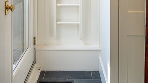 En smal gang med en hvid dør til venstre, en hvid dør til højre og et hvidt reolsystem i midten.