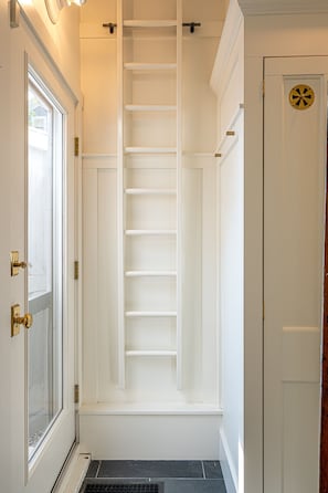 A narrow hallway with a white door on the left, a white door on the right, and a white shelf unit in the center.