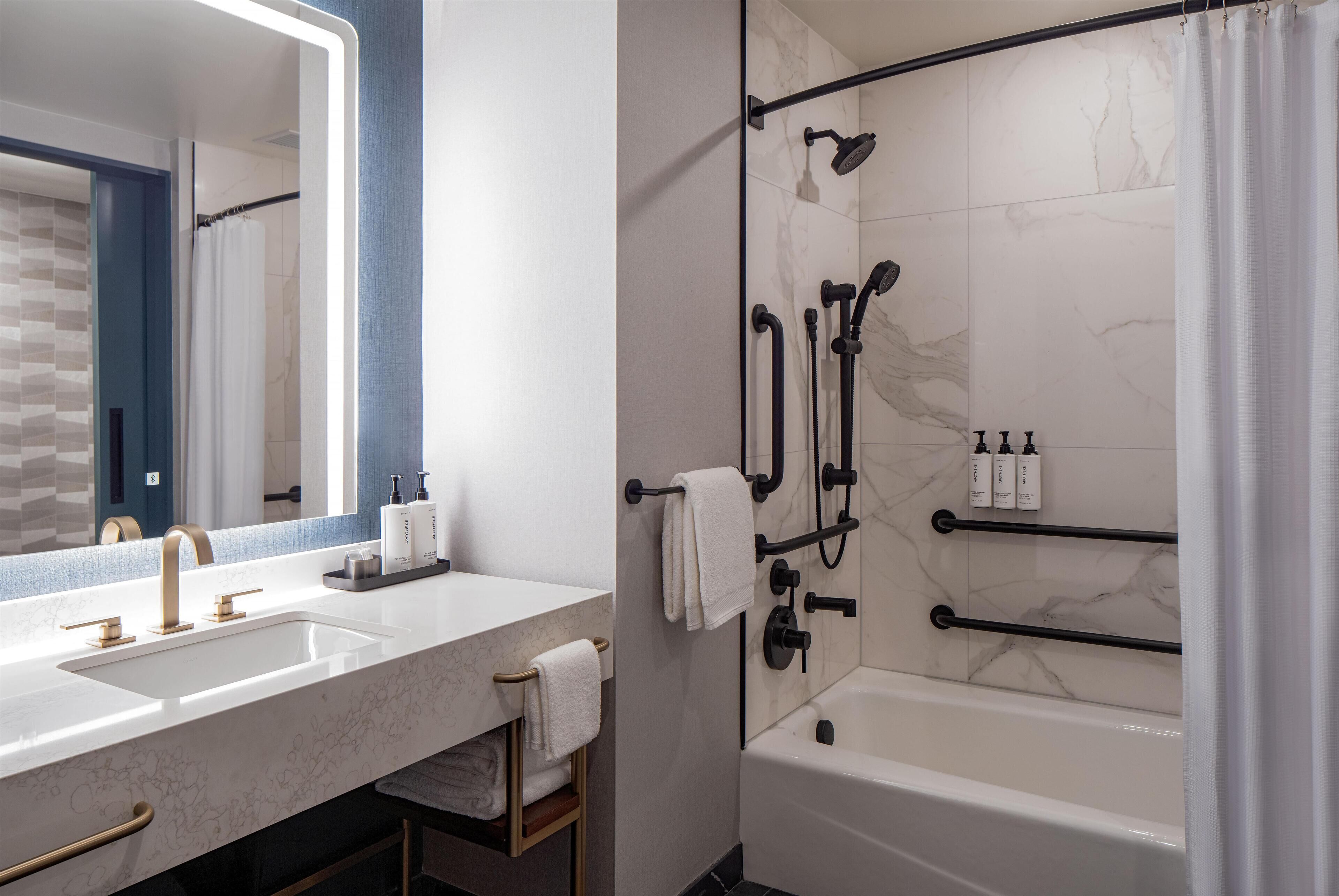 A modern bathroom with a large mirror, dual sinks, a bathtub, and a shower with a glass door.