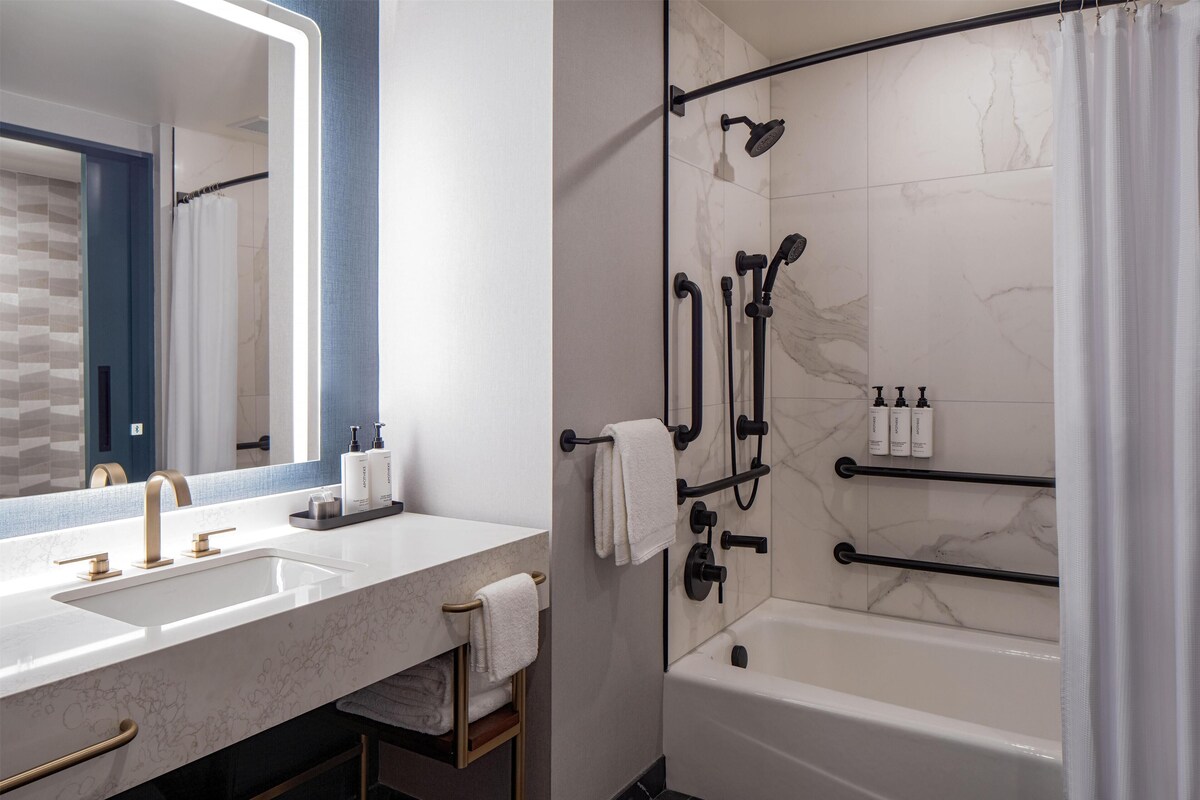 A modern bathroom with a large mirror, dual sinks, a bathtub, and a shower with a glass door.