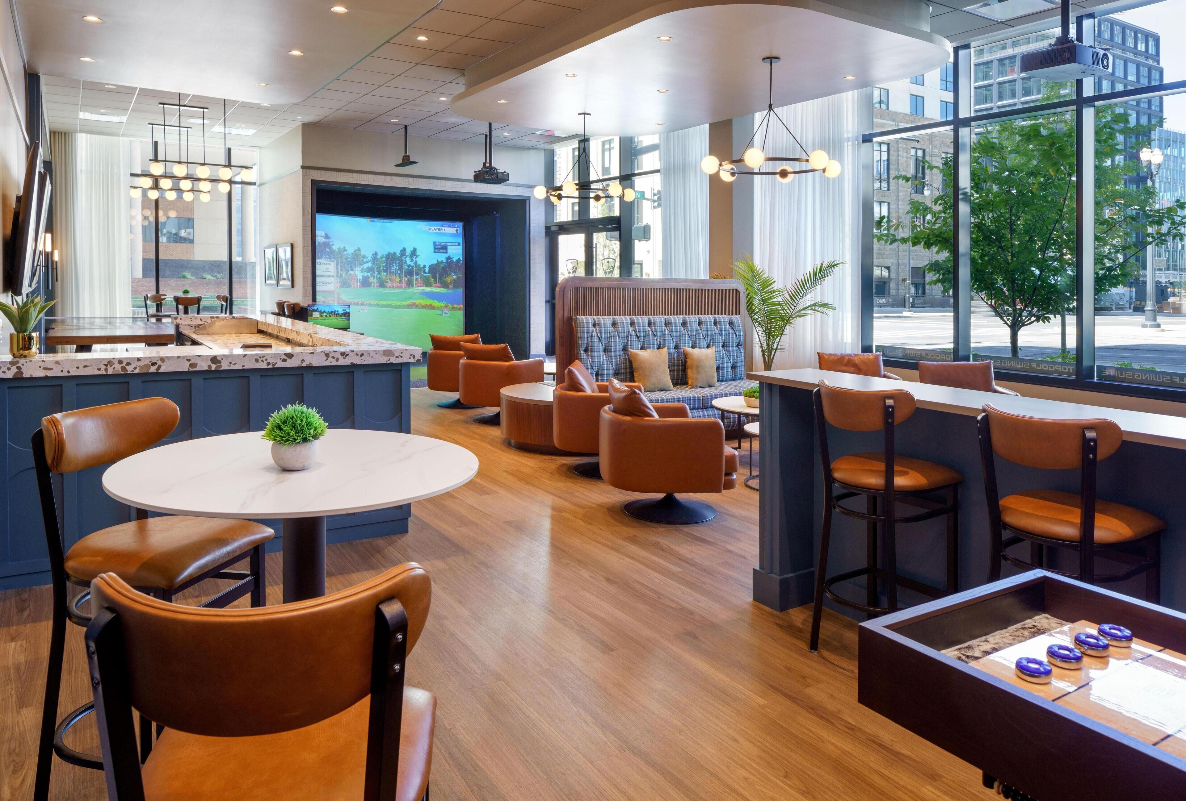 A modern hotel lobby with a bar area, seating arrangements, and large windows offering city views.