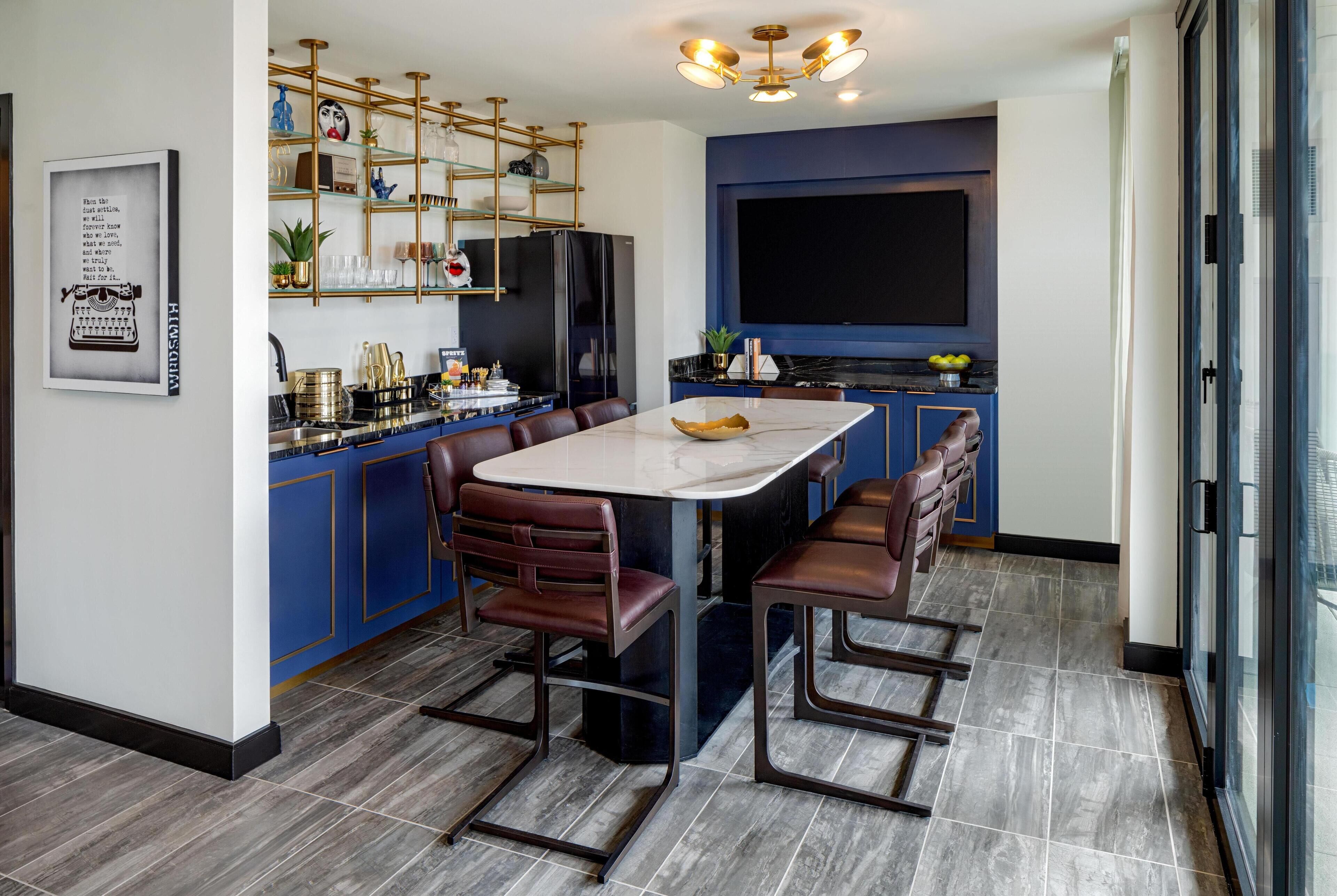 Una cocina moderna con una isla de mármol, armarios azules y un televisor grande.