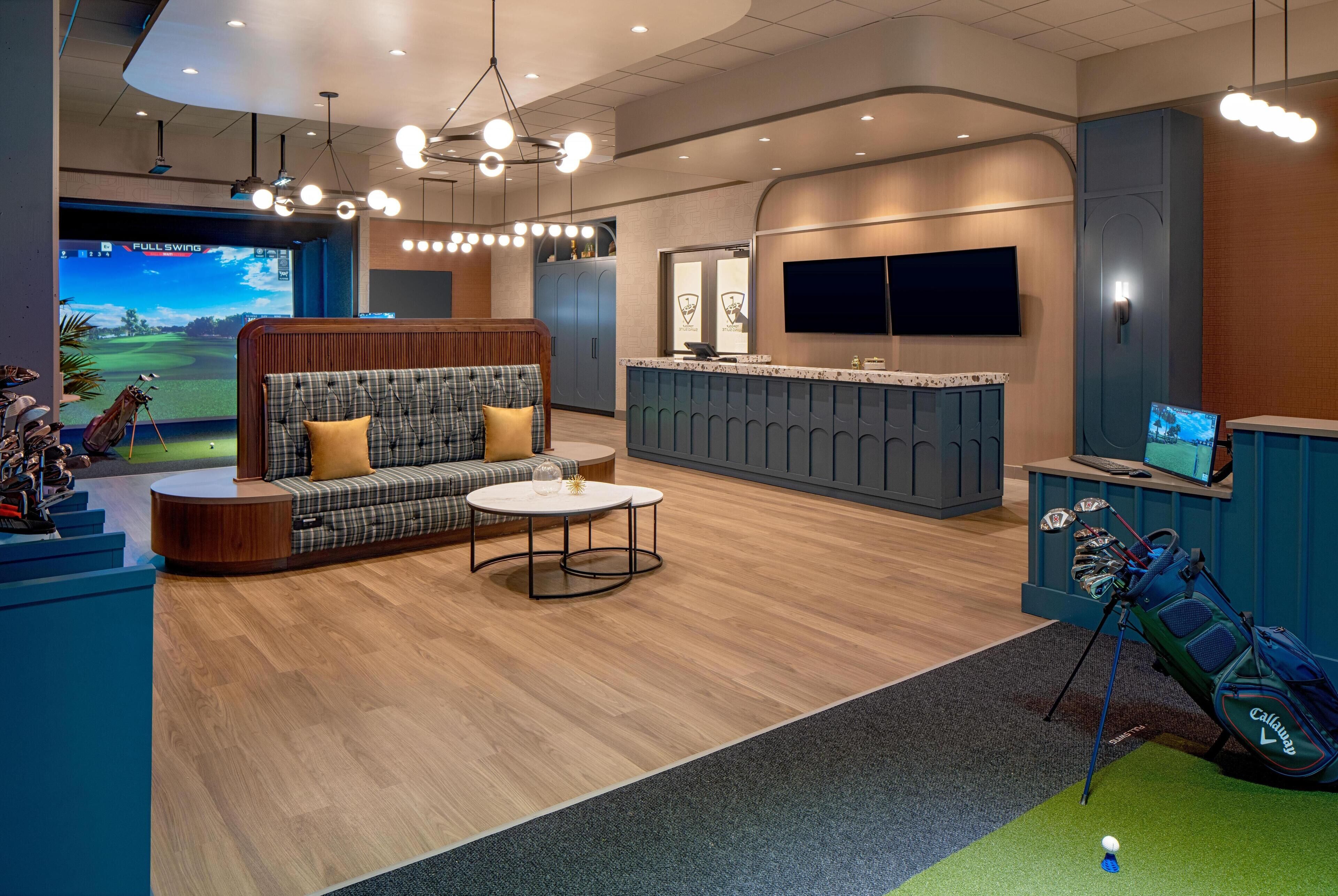 A modern indoor golf simulation area with a seating area, a reception desk, and a golf cart.