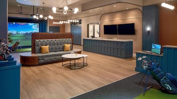 A modern indoor golf simulation area with a seating area, a reception desk, and a golf cart.