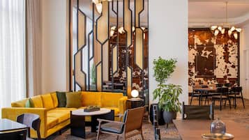 Um hall de hotel moderno com um sofá amarelo, uma mesa redonda e uma área de refeições com cadeiras.