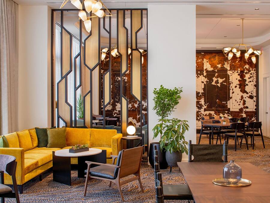 Um hall de hotel moderno com um sofá amarelo, uma mesa redonda e uma área de refeições com cadeiras.