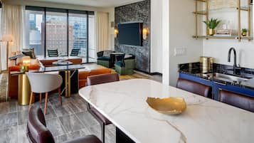 Una habitación de hotel moderna con una amplia mesa de comedor, asientos cómodos, una zona de cocina y vistas a la ciudad.