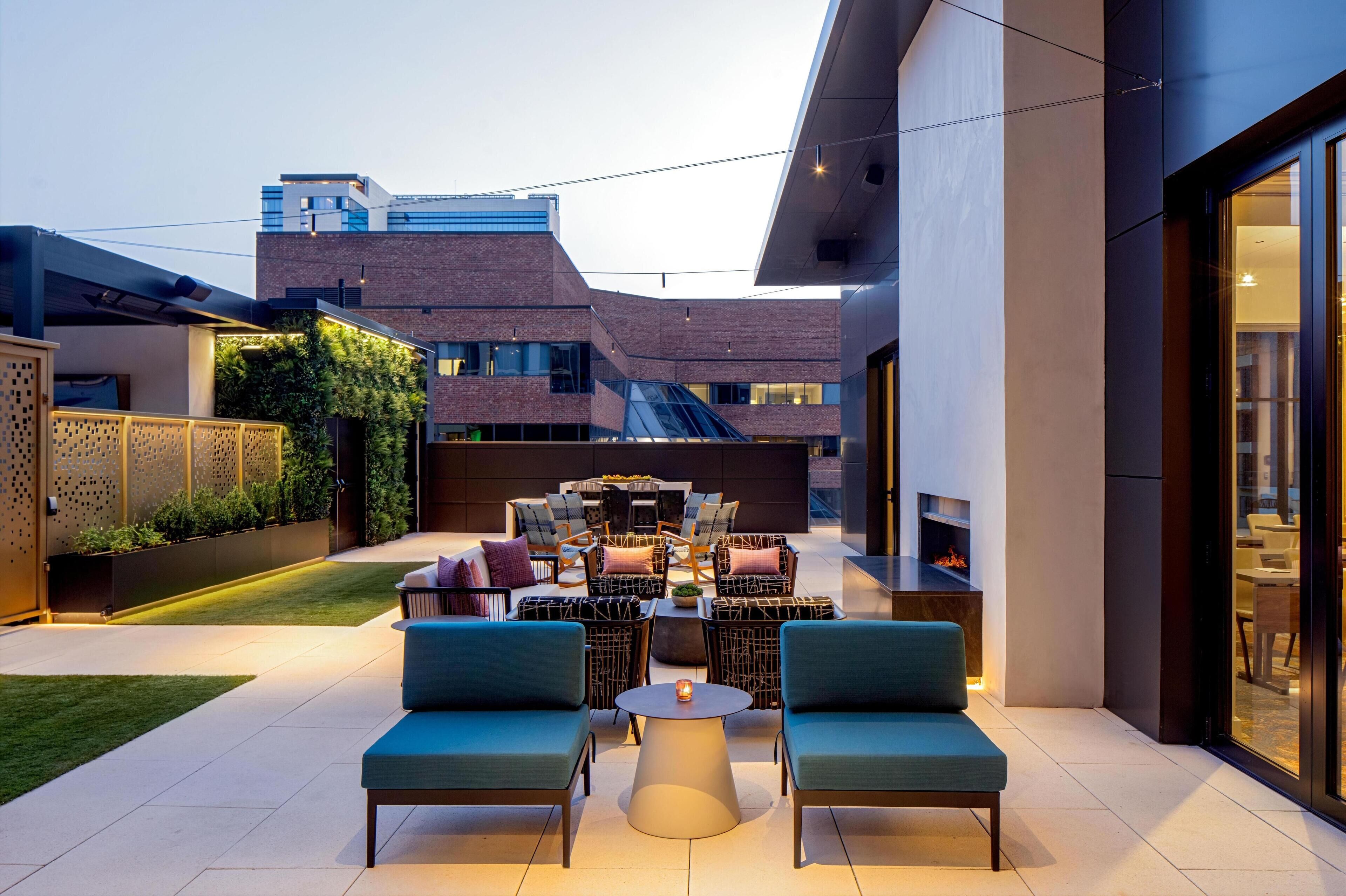 An outdoor patio area with seating, a fire feature, and a view of a modern building in the background.