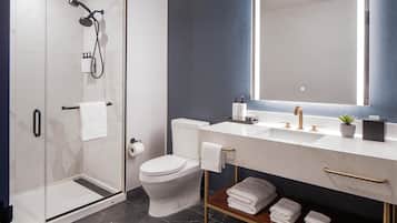 Un baño moderno con ducha de vidrio, inodoro, lavamanos con espejo y estante con toallas dobladas.