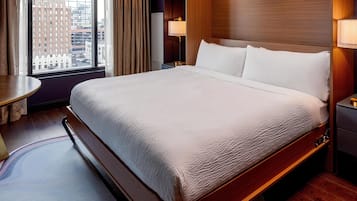 A hotel room with a large bed, a bedside table, a lamp, and a view of the city through the window.