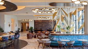 A modern lobby with a reception desk, seating area, and a large window with geometric patterns. - Tempo By Hilton Nashville Downtown (Nashville)
