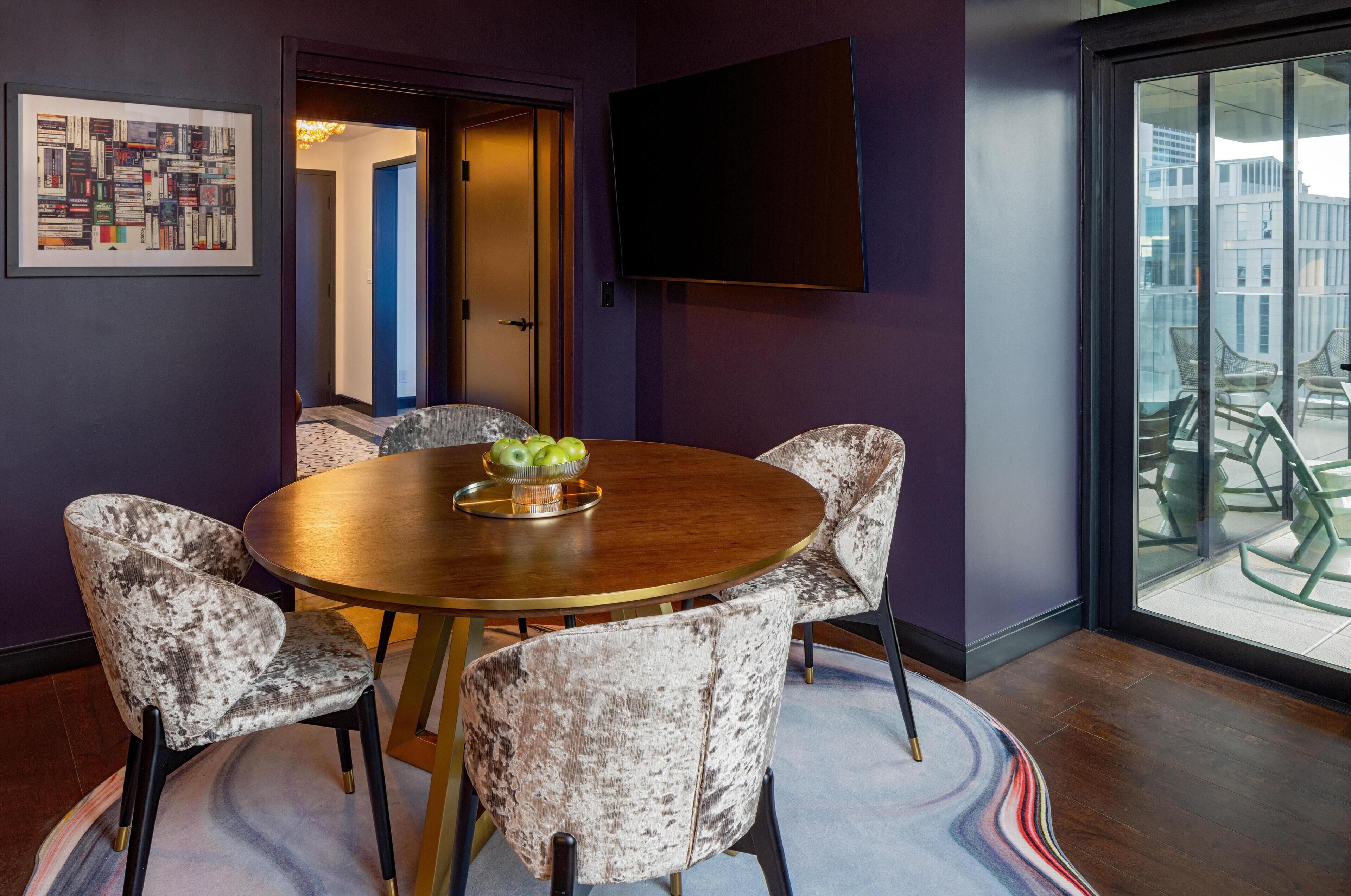 Une salle de conférence avec une table ronde, six chaises, un panier de fruits, un tableau encadré, un téléviseur et une vue sur le balcon extérieur.