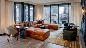 A spacious living room with a large sofa set, a dining table, and a view of the cityscape through large windows. - Tempo By Hilton Nashville Downtown (Nashville)