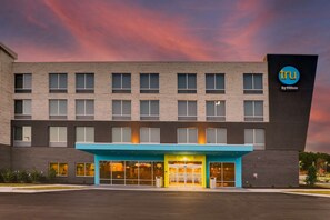 Ein modernes Hotel mit einem gut sichtbaren 'tru by Hilton' Schild, das eine Backsteinfassade, zahlreiche Fenster und einen blauen Eingangsbereich aufweist.