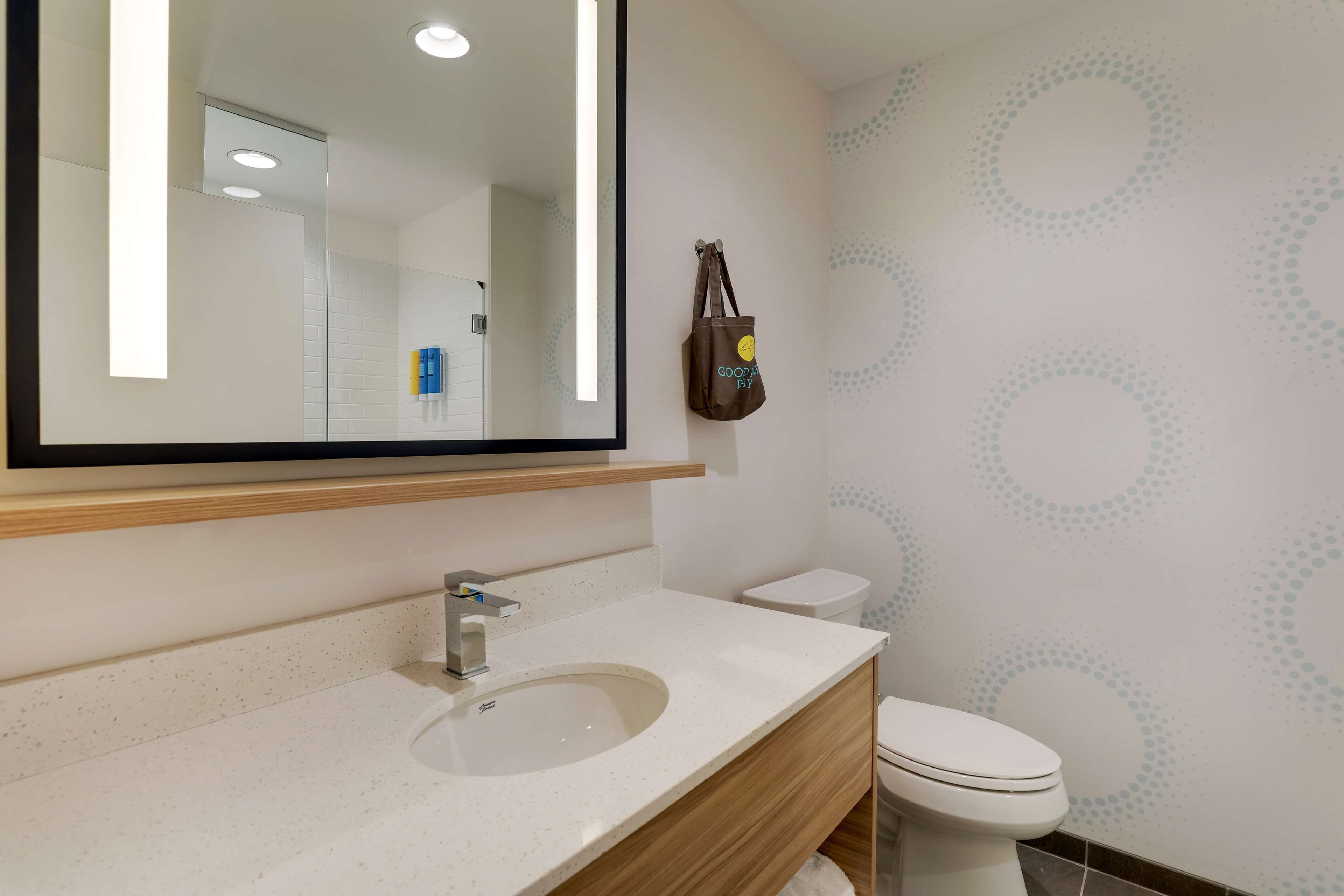 A bathroom with a large mirror, a sink, a toilet, and a wall with a circular pattern.