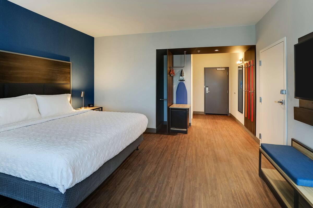 Ein Hotelzimmer mit einem großen Bett, Holzboden, einer Sitzecke mit einer Bank und einem an der Wand befestigten Fernseher.