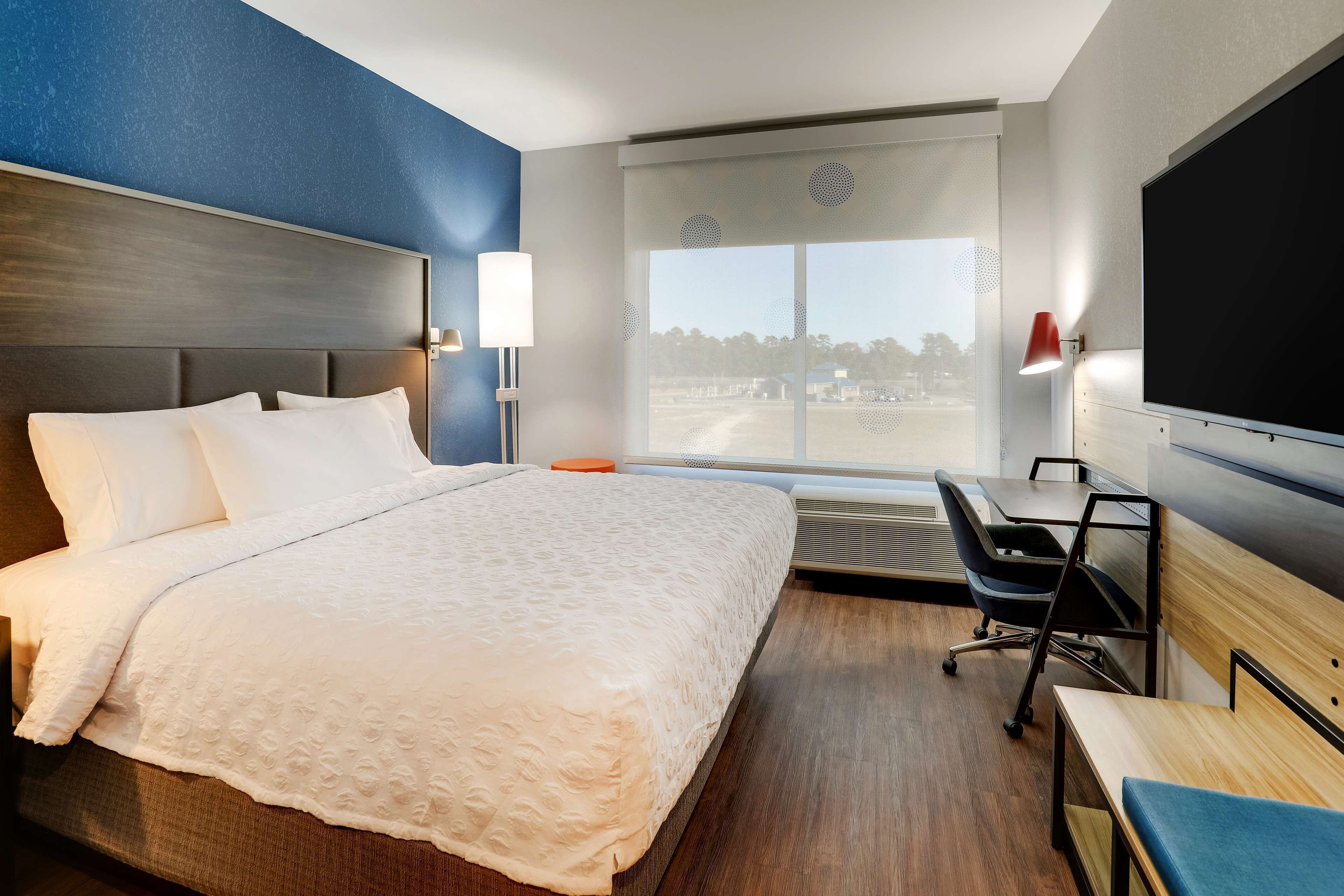 Une chambre d’hôtel avec un grand lit, un bureau, une chaise, une télévision et une fenêtre donnant sur l’extérieur.
