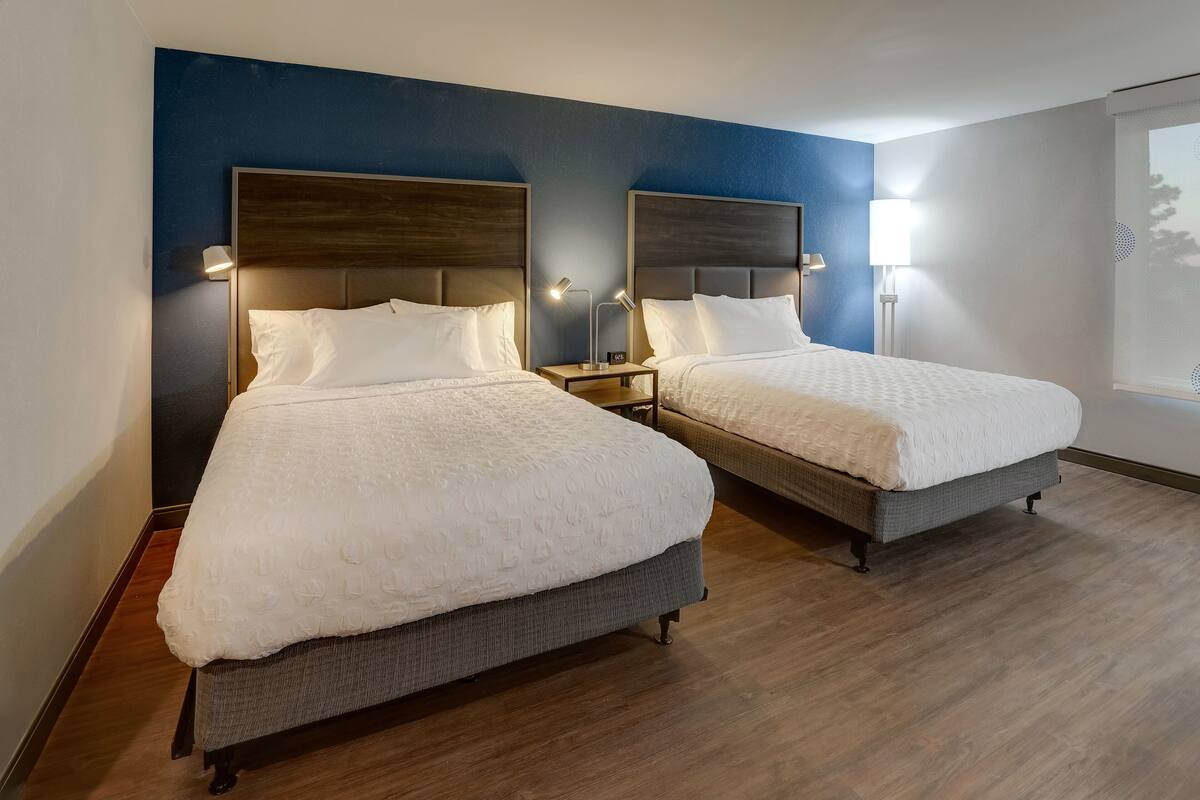 Ein Hotelzimmer mit zwei Betten, jeweils mit einem Holz-Kopfstück und Nachttischlampen.