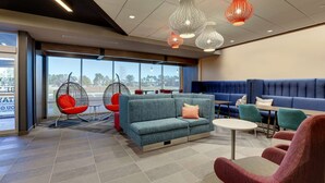 Un espace de détente moderne avec un canapé bleu, des fauteuils rouges et un coin salon bleu. Des guirlandes lumineuses rouges et blanches sont suspendues, et une grande fenêtre offre une vue sur les arbres.