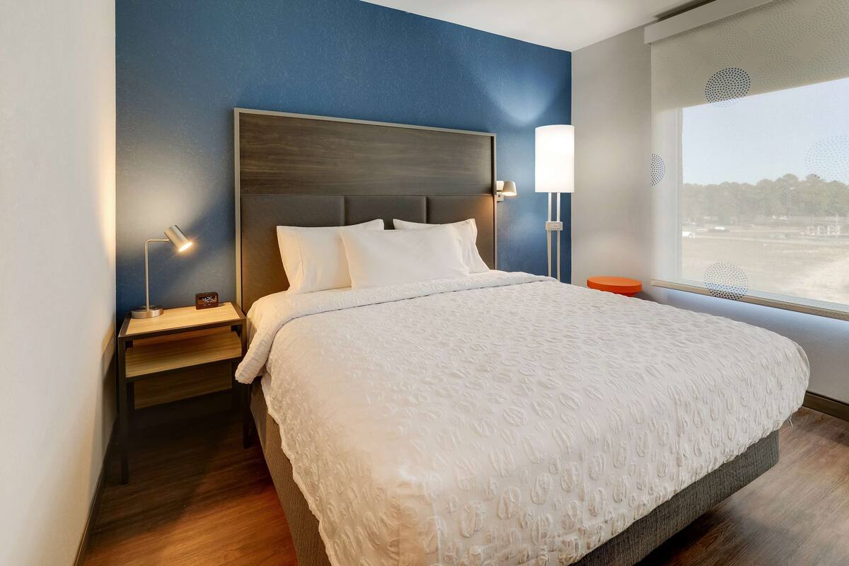 Ein ordentlich bezogenes Bett mit weißer, strukturierter Bettdecke, einem Holz-Kopfteil und zwei Nachttischlampen.