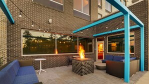Une terrasse extérieure dotée d’un foyer en briques, de sièges bleus et d’un espace couvert avec des colonnes bleues.