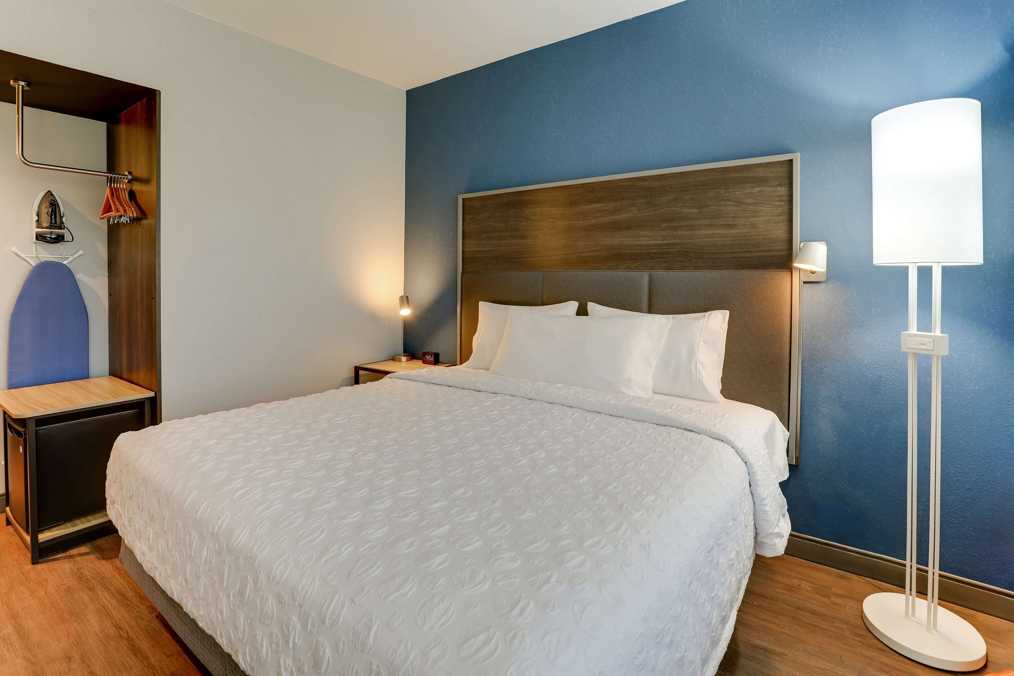 Quarto de hotel com uma cama grande, mesa de cabeceira, espelho, porta-toalhas na parede e abajur.