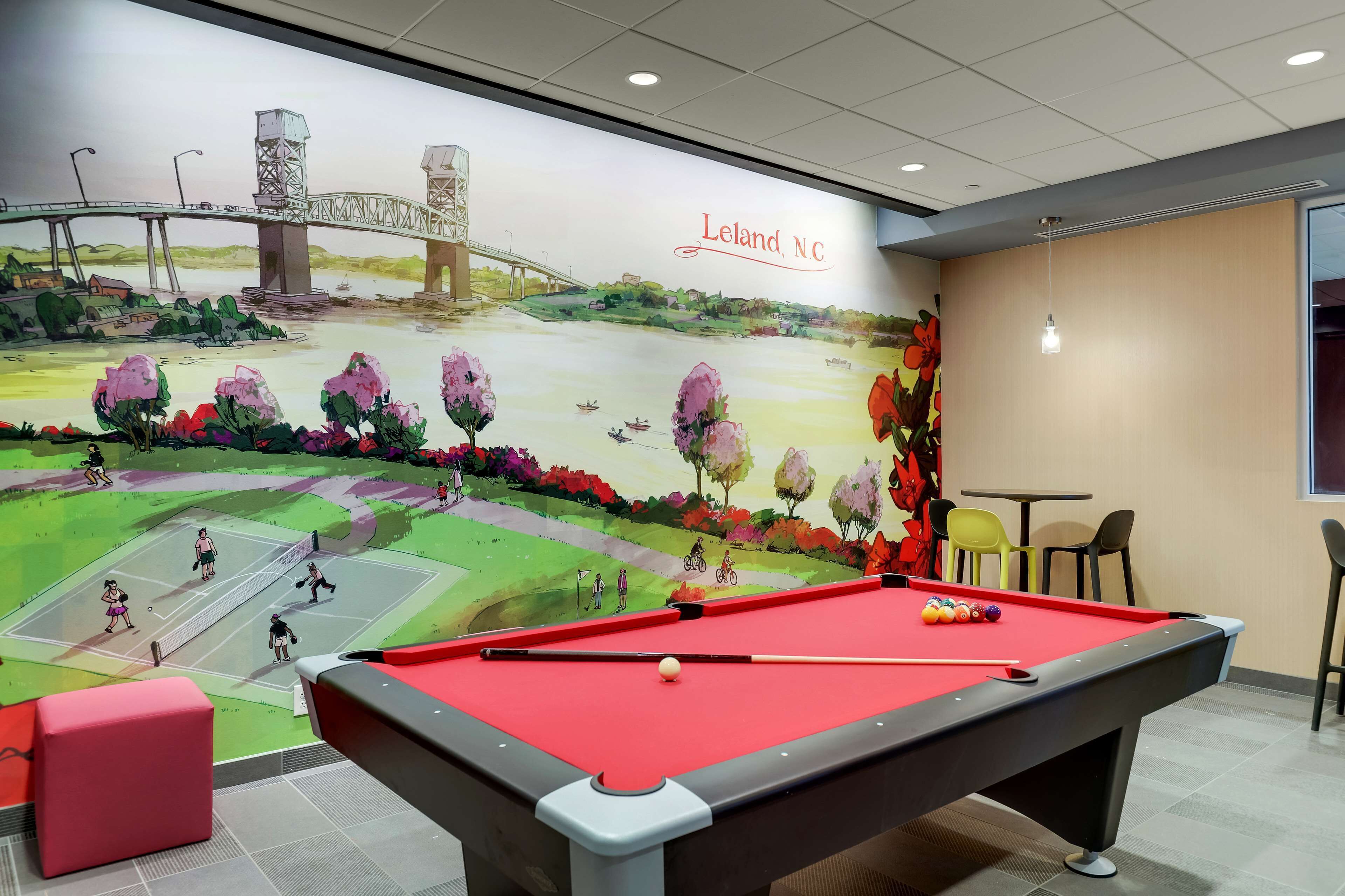 Une table de billard dans une pièce ornée d’une fresque représentant un pont, avec une pancarte indiquant « Leland, Caroline du Nord ».