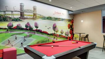 Une table de billard dans une pièce ornée d’une fresque représentant un pont, avec une pancarte indiquant « Leland, Caroline du Nord ».