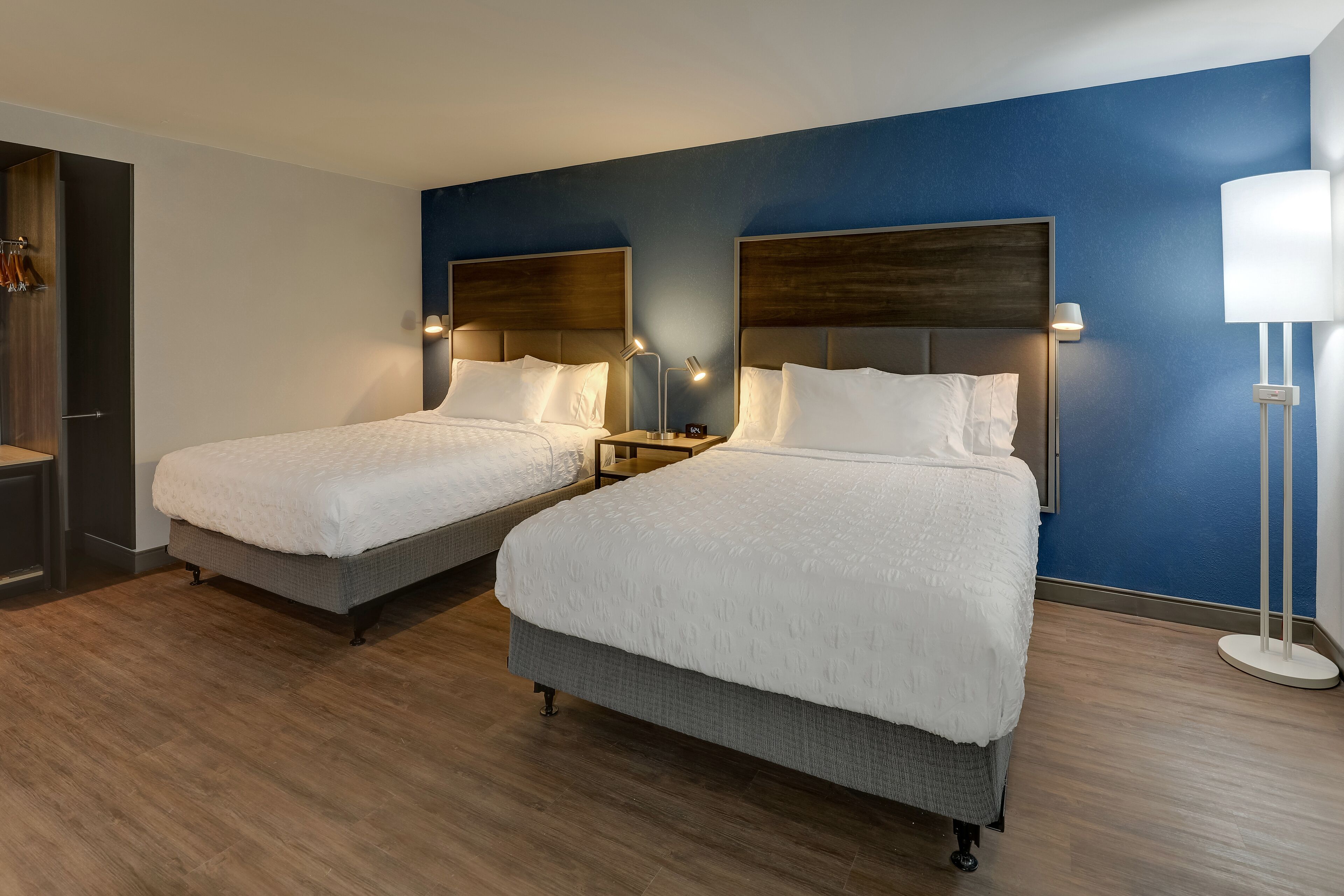 A hotel room with two beds, wooden flooring, and a blue accent wall.