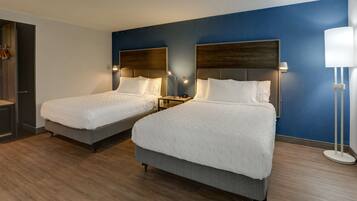 A hotel room with two beds, wooden flooring, and a blue accent wall.