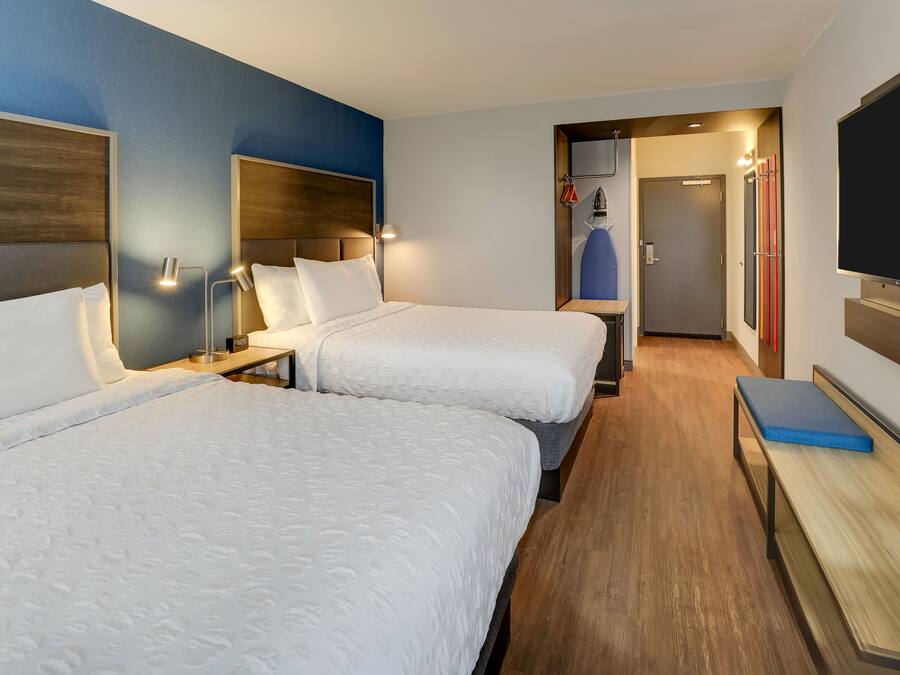 A hotel room with two beds, a TV, a desk, and a bench.