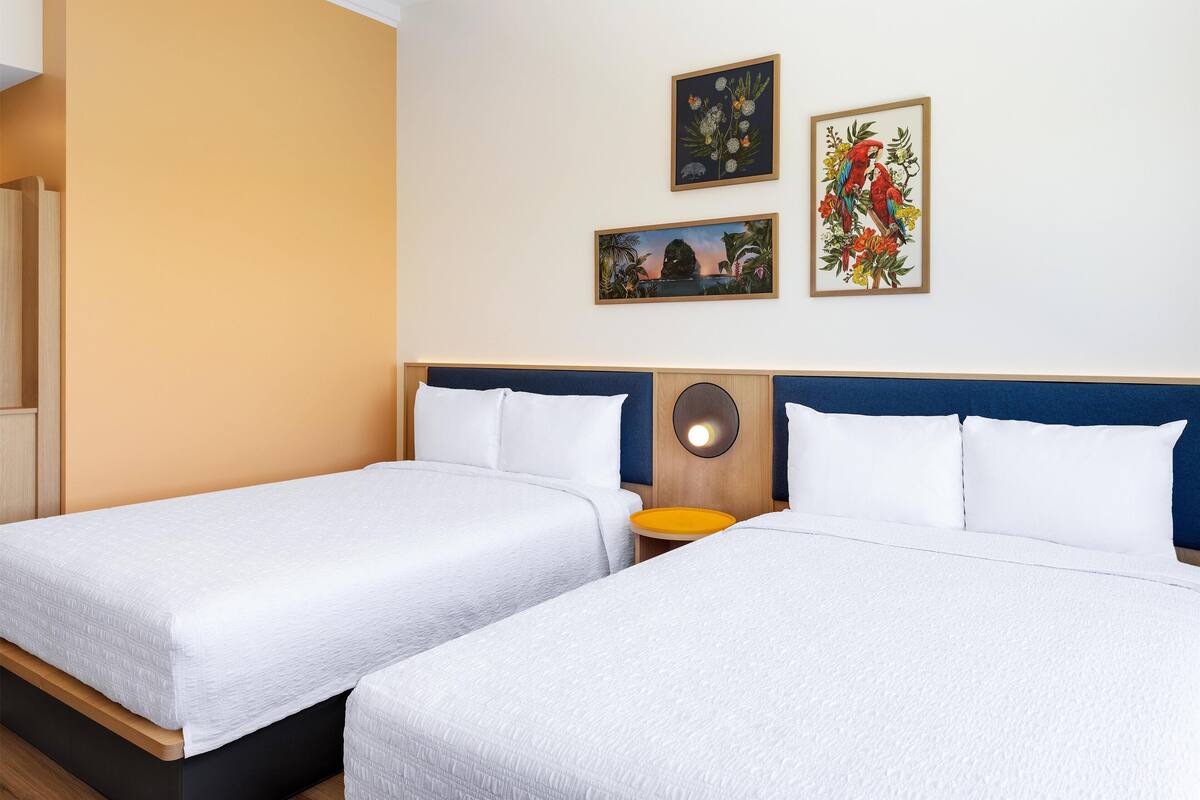 Ein Hotelzimmer mit zwei Einzelbetten, einem Holz-Kopfteil, einem kleinen runden Tisch und drei gerahmten Bildern an der Wand.