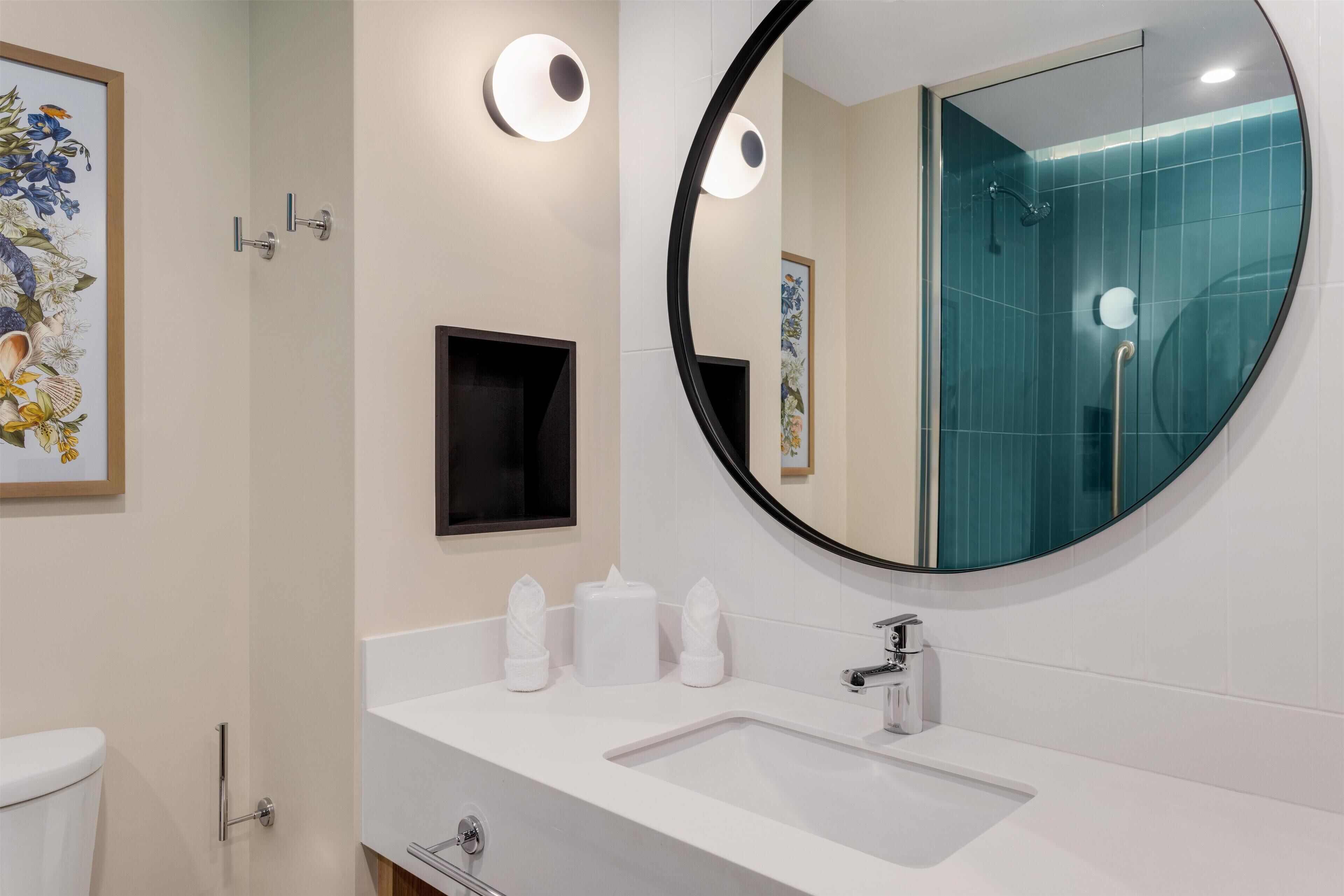 A modern bathroom with a round mirror, white sink, and a glass shower enclosure.