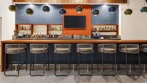 A bar area with a long counter, multiple stools, and shelves stocked with bottles.
