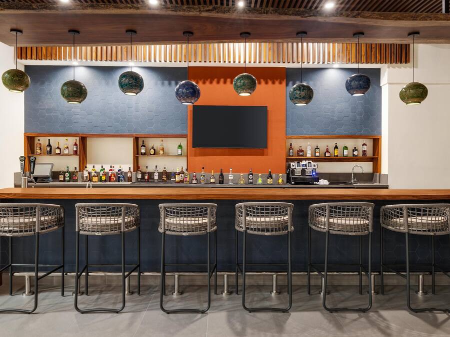 A bar area with a long counter, multiple stools, and shelves stocked with bottles.
