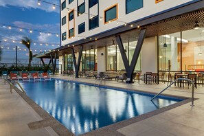 A modern hotel with a swimming pool, outdoor seating, and string lights.