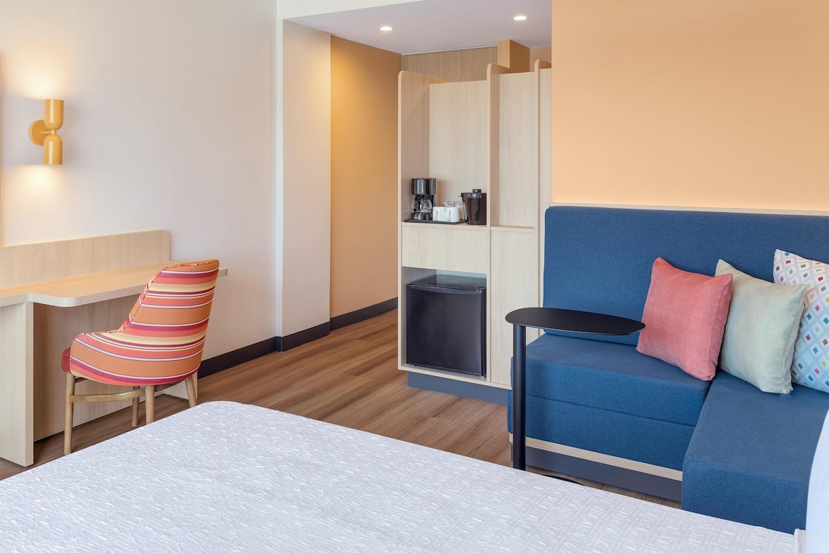 Ein Hotelzimmer mit einem Bett, einem blauen Sofa, einem gestreiften Sessel, einem Schreibtisch und einer Küchenzeile.
