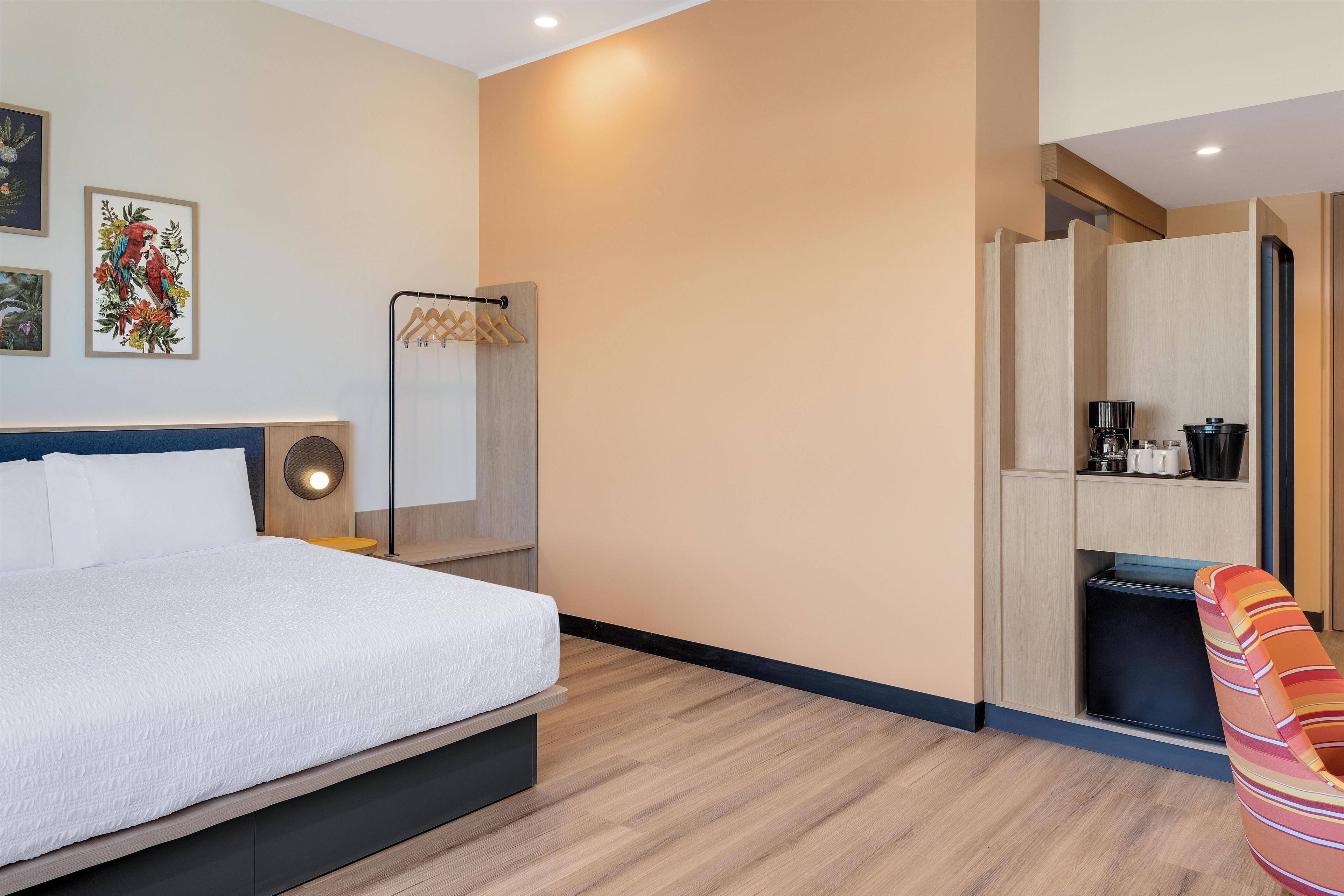 A bedroom with a bed, a wardrobe, a small kitchenette, and a chair.