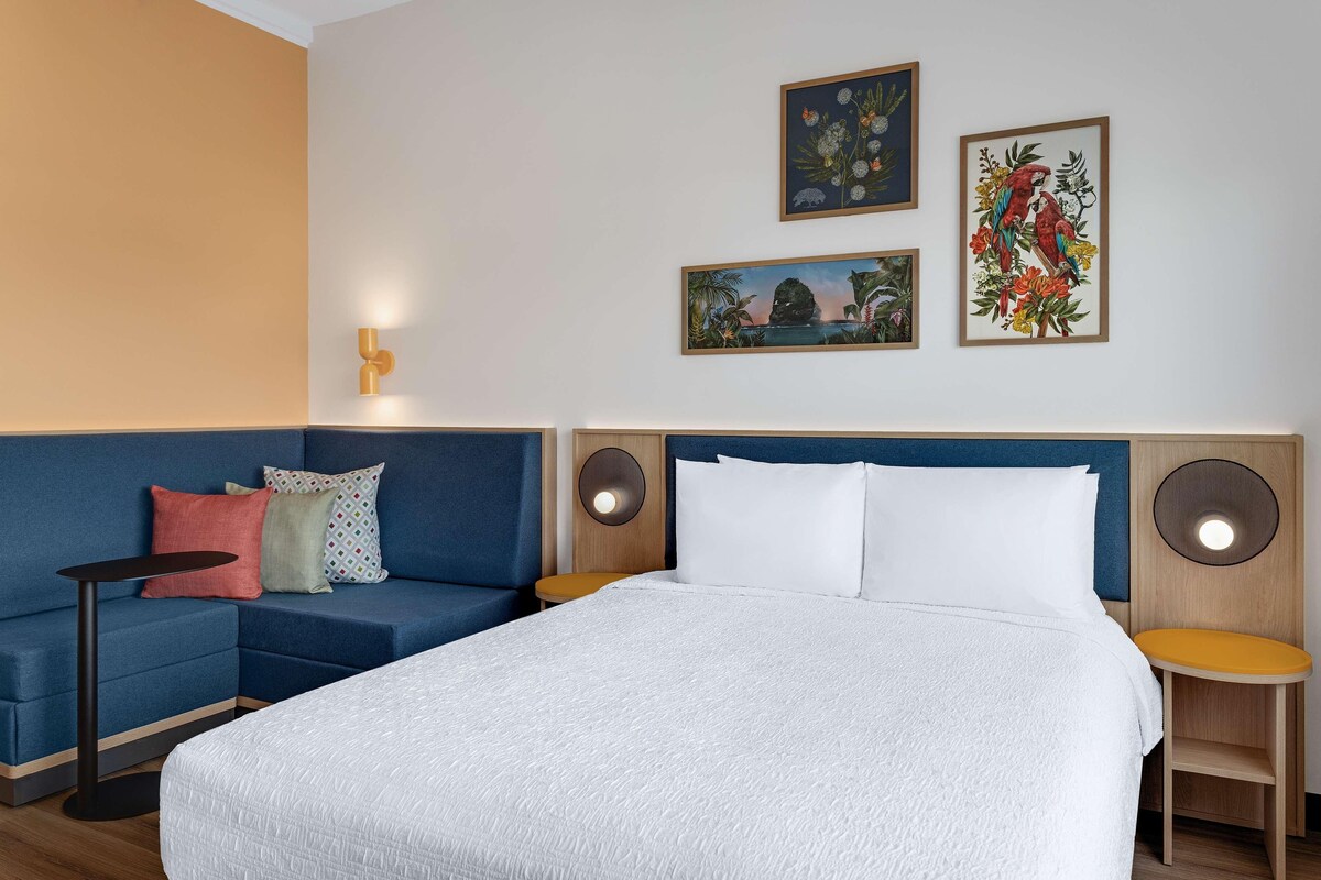 Une chambre d’hôtel avec un lit, un canapé bleu, une petite table et deux haut-parleurs fixés au mur.