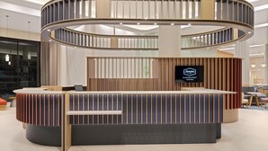 A modern reception desk with a curved design, a flat-screen TV, and a sign indicating the location as Hampton Guanacaste Airport, Costa Rica.